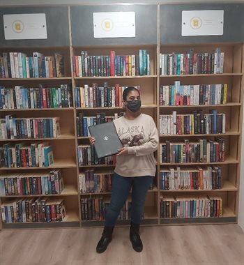 Young lady posing with laptop in front of bookshelves full of books